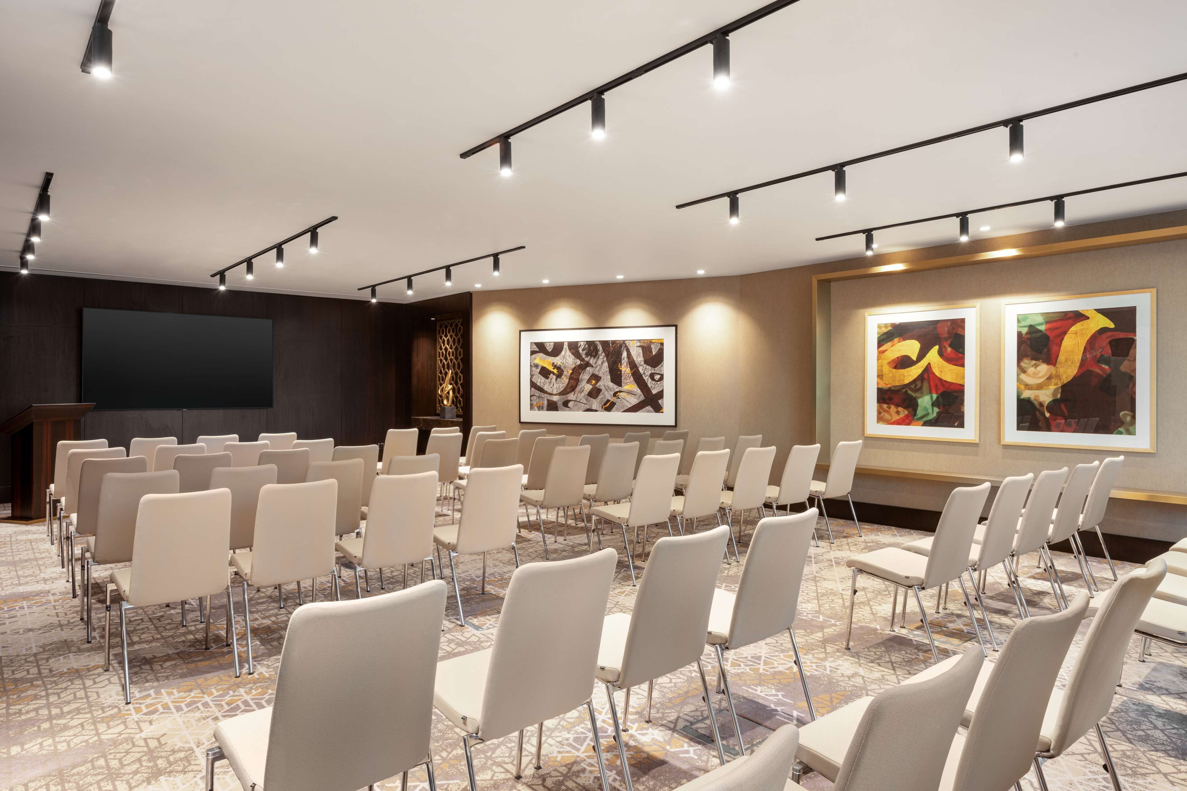 A conference room with rows of chairs, a podium, and framed artwork on the walls.