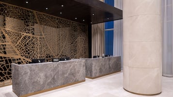 Un espace d’accueil au design moderne, comprenant un comptoir de réception en marbre et un mur décoratif orné d’un motif géométrique.
