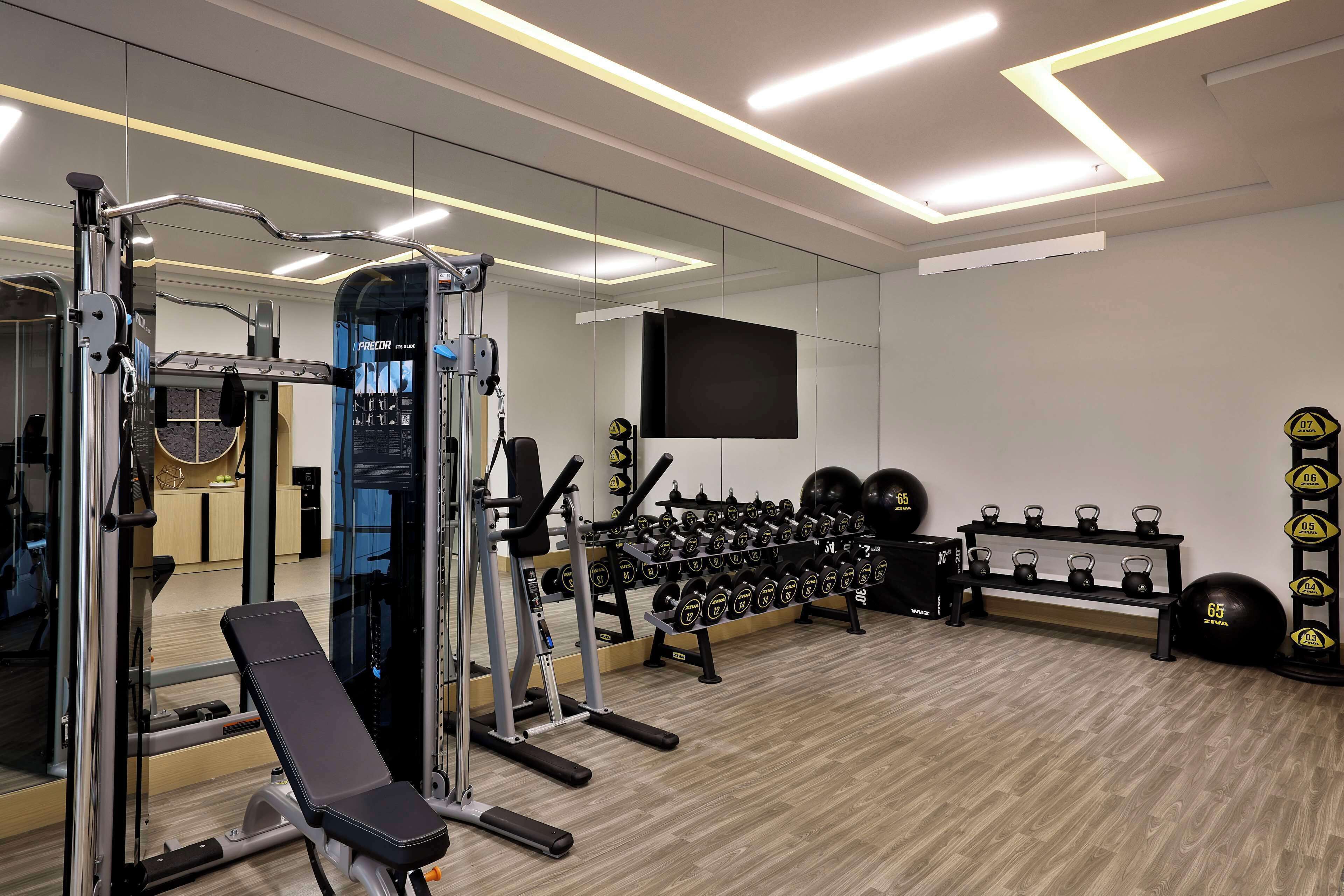 A gym with exercise equipment, a bench, a mirror, a TV, and a weight rack.