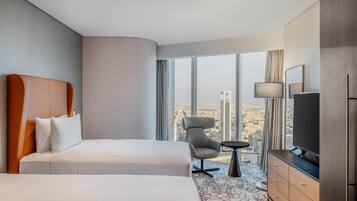Ein Hotelzimmer mit zwei Betten, einem Fernseher, einem kleinen Tisch und einem Sessel.