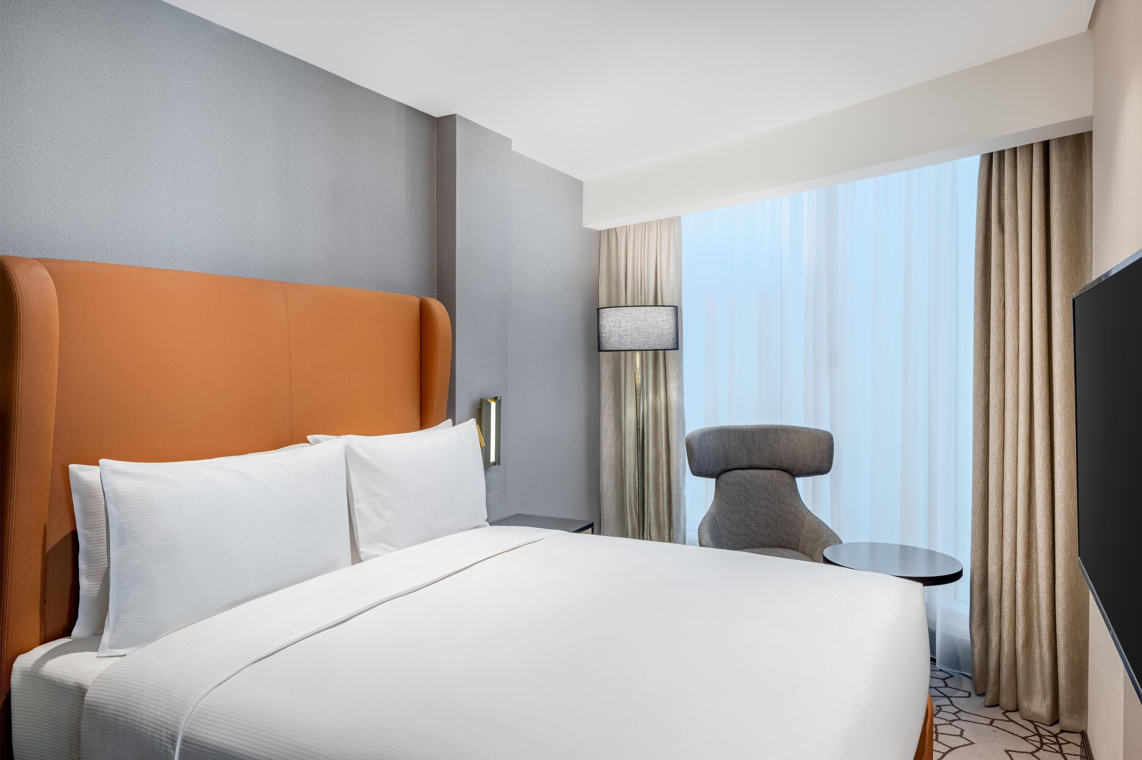 Ein Hotelzimmer mit einem großen Bett, einem Sessel, einem kleinen Tisch und einem Fernseher.