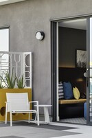 Un área de estar moderna al aire libre con un banco blanco y una mesita, una planta en maceta y un panel decorativo en la pared.