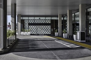 A modern hotel entrance with a geometric facade, a parking area, and a reception desk. - Hilton Buena Park Anaheim (Buena Park)