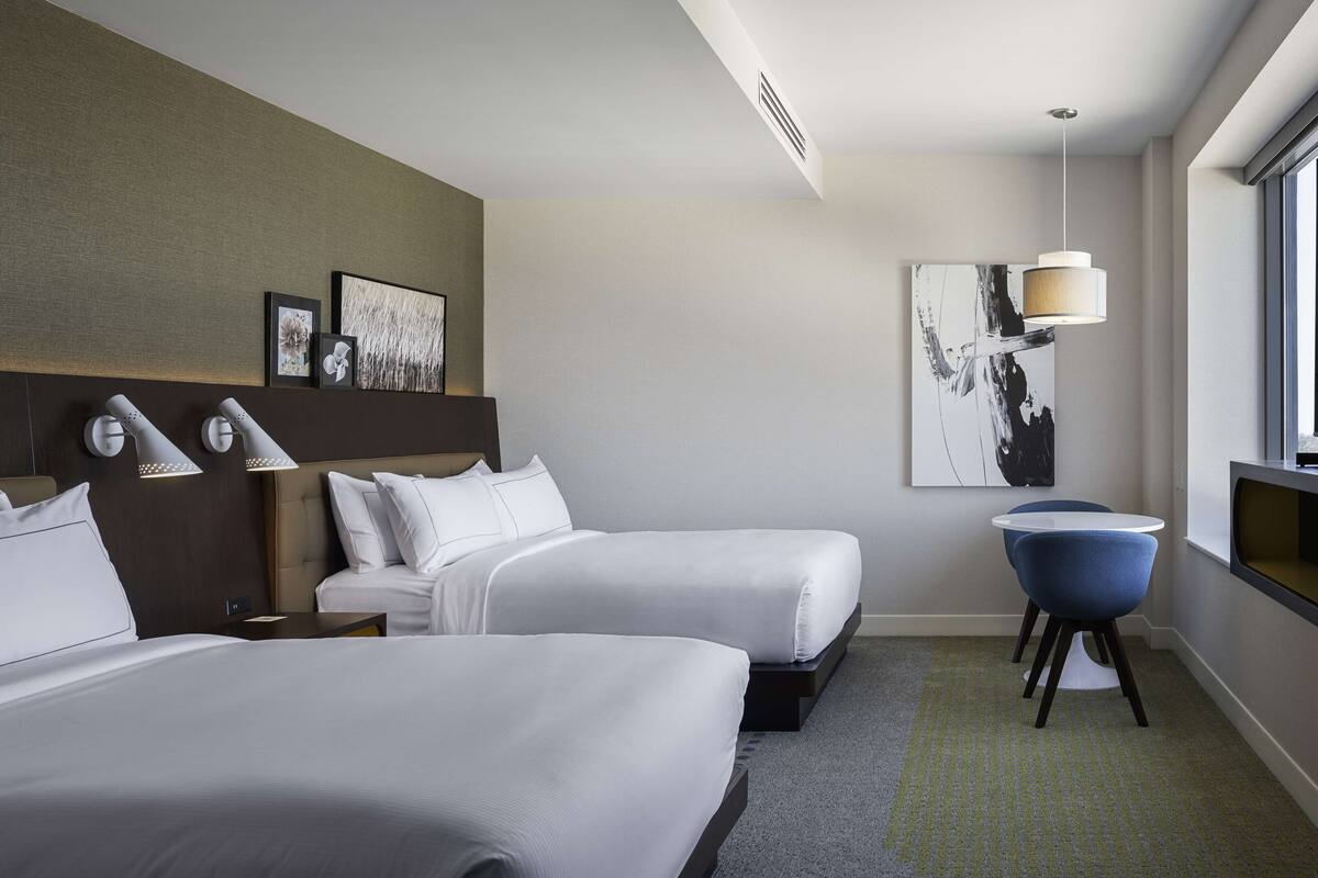 Een hotelkamer met twee bedden, een bureau, een stoel en kunst aan de muren.