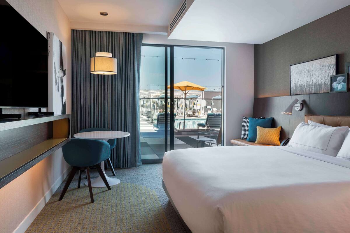 Hotelkamer met een groot bed, een televisie, een bureau met stoel en een balkon met buitenmeubilair.