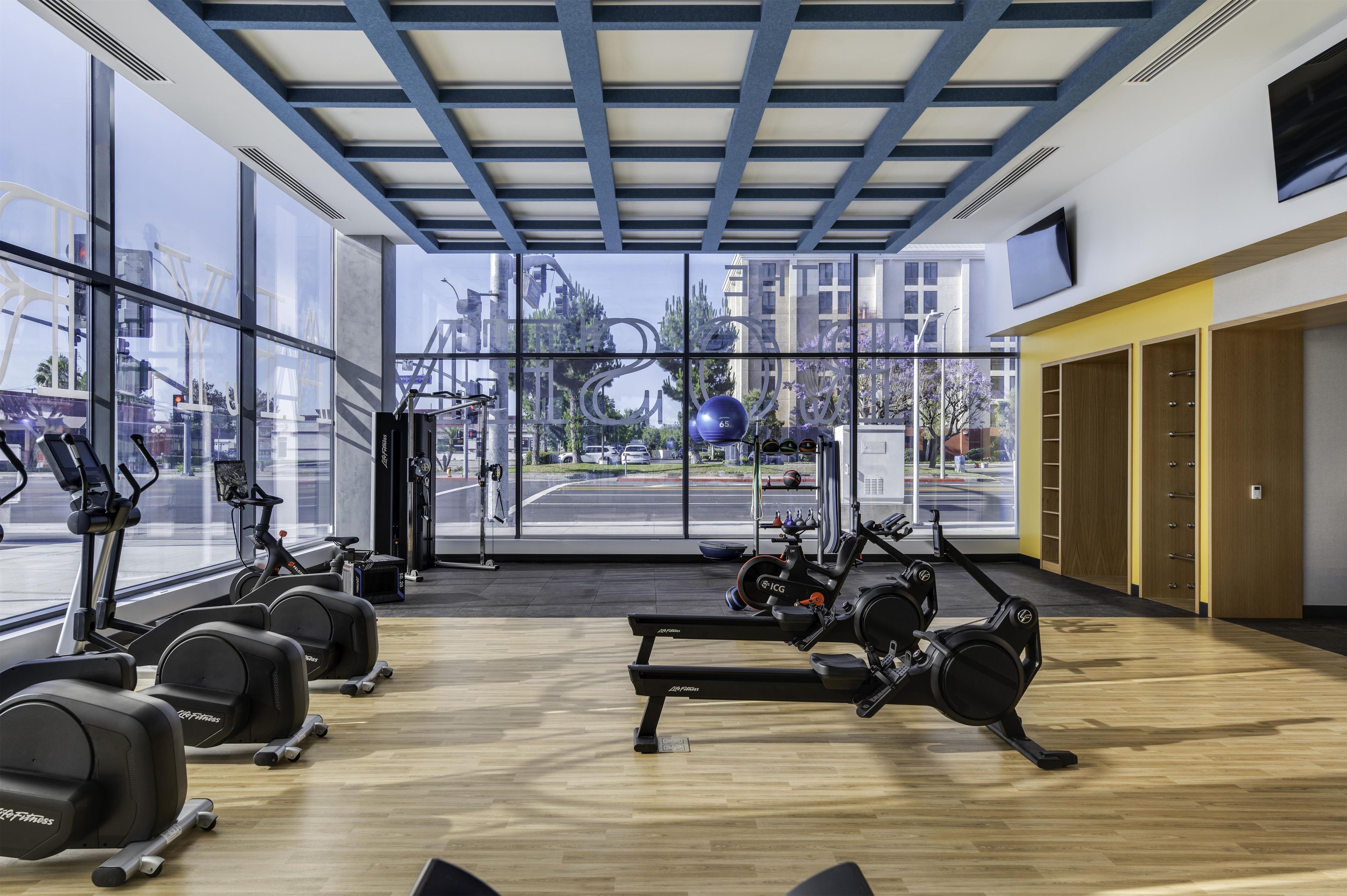 A gym with exercise equipment, large windows, and a view of the street.