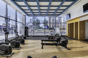 Un gimnasio con equipo de ejercicio, ventanas amplias y vista a la calle.
