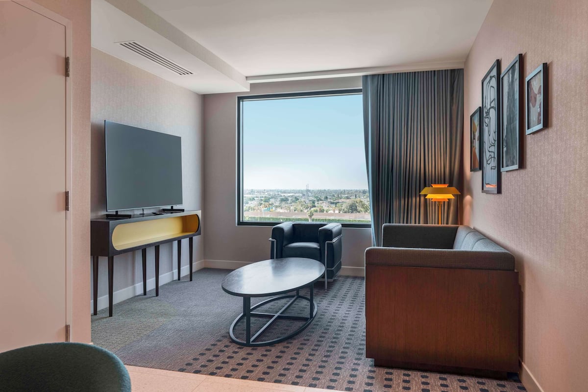 Een hotelkamer met een groot raam, een flatscreen televisie, een bank, een kleine tafel en een lamp.