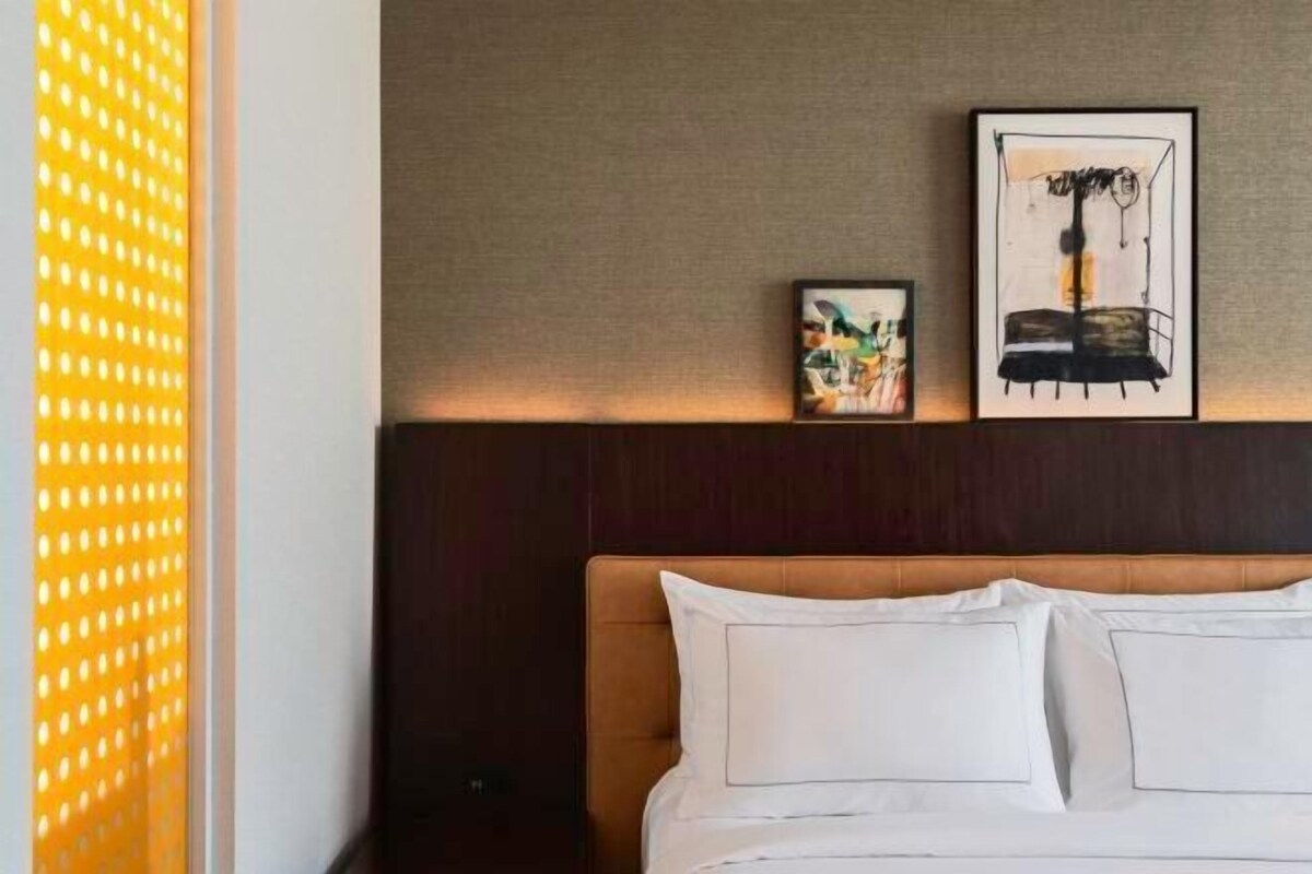 A bed with white linens, a wooden headboard, and two framed artworks on the wall.