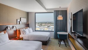 Ett hotellrum med två sängar, en TV, ett skrivbord och utsikt över staden.