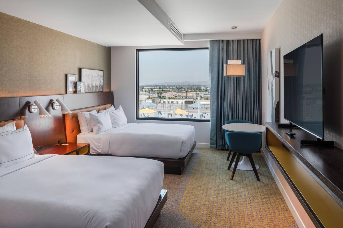 Een hotelkamer met twee bedden, een televisie, een bureau en uitzicht op de stad.