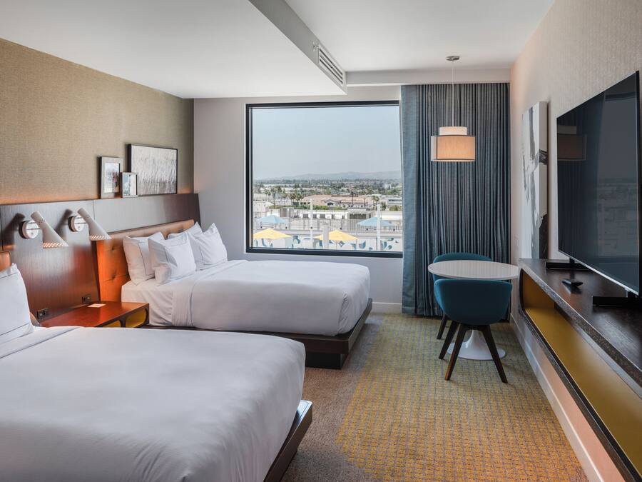 Ein Hotelzimmer mit zwei Betten, einem Fernseher, einem Schreibtisch und Blick auf die Stadt.