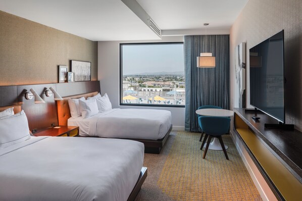 Une chambre d’hôtel avec deux lits, une télévision, un bureau et une vue sur la ville.