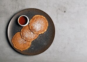Une assiette avec trois crêpes et une petite tasse de sirop.