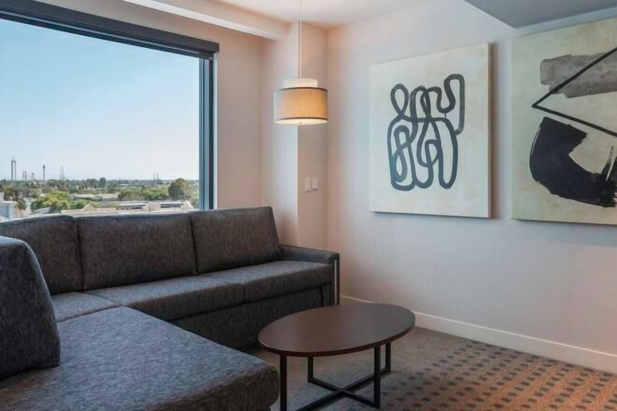 A modern hotel room with a gray sofa, a small round table, and abstract wall art.