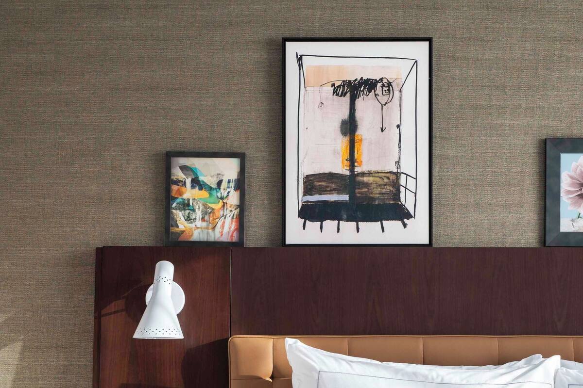 Een hotelkamer met een bed, een nachtkastje met een lamp en kunst aan de muur.