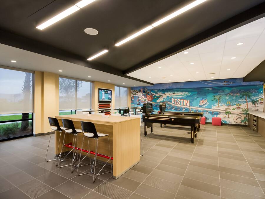 A modern indoor space with a reception desk, bar area, and a mural depicting a beach scene.