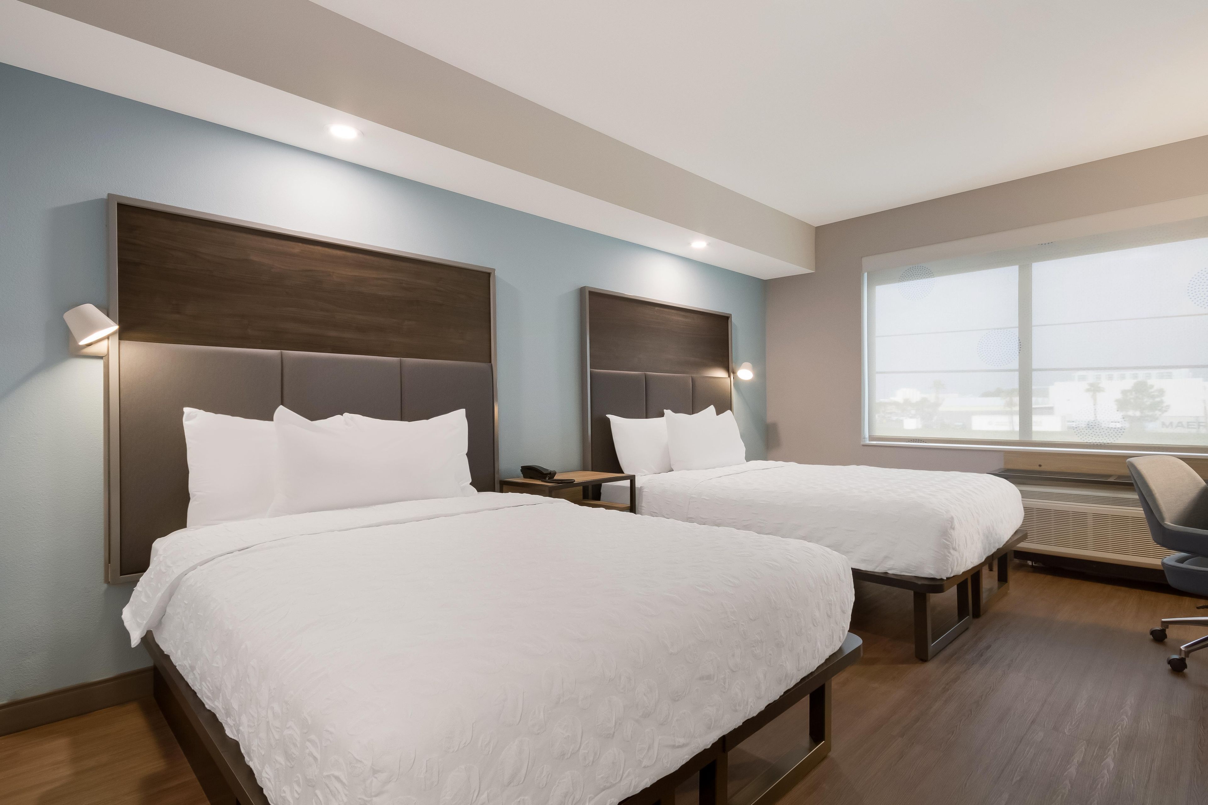 A hotel room with two beds, a desk, a chair, and a large window.