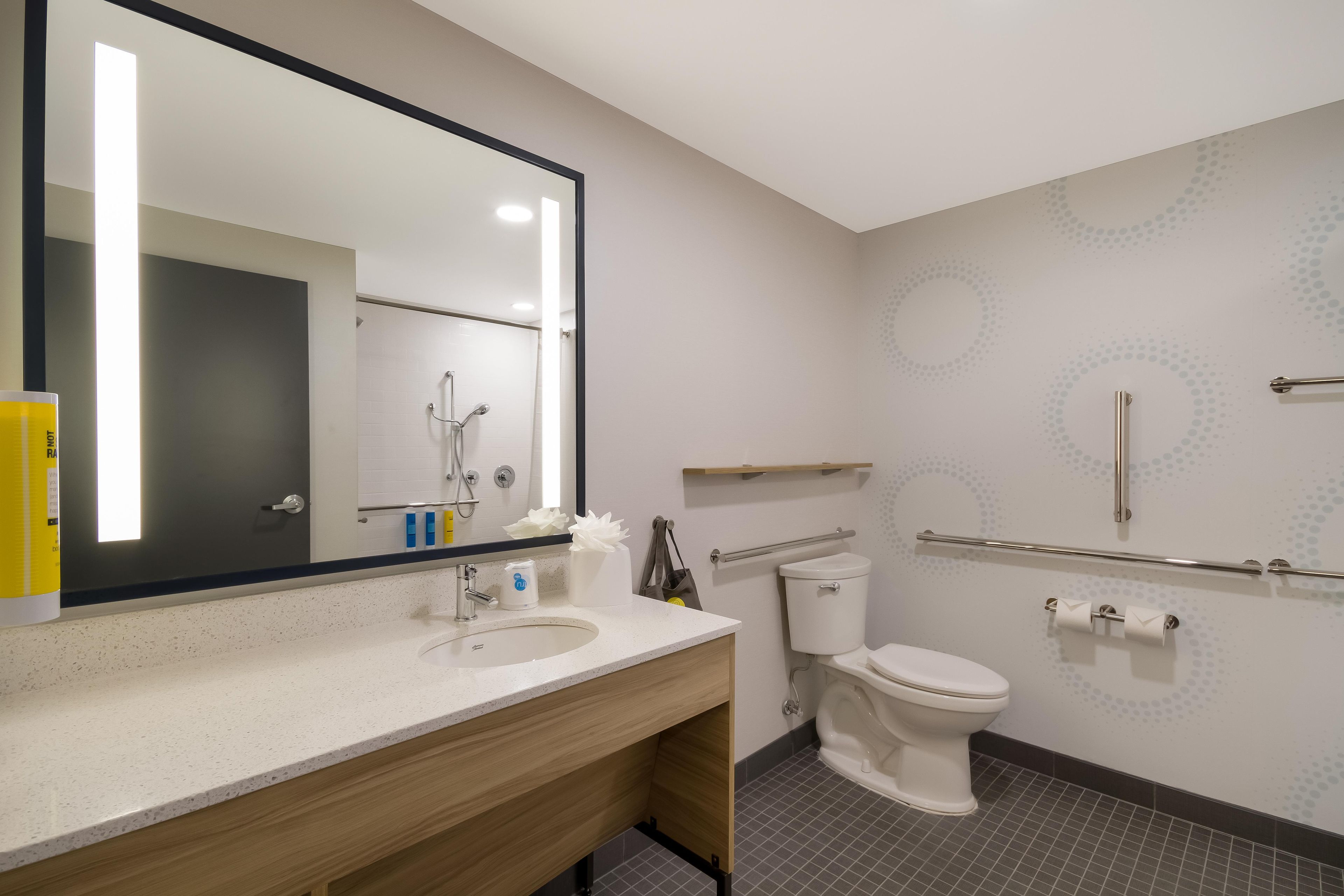 A modern bathroom with a large mirror, a sink with a wooden vanity, a toilet, and a shower area.