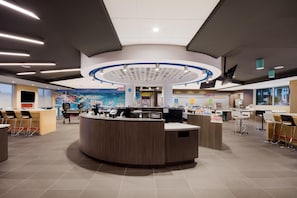 A modern hotel lobby with a central reception desk, multiple seating areas, and a large mural on the wall. - Tru By Hilton Destin (Destin)