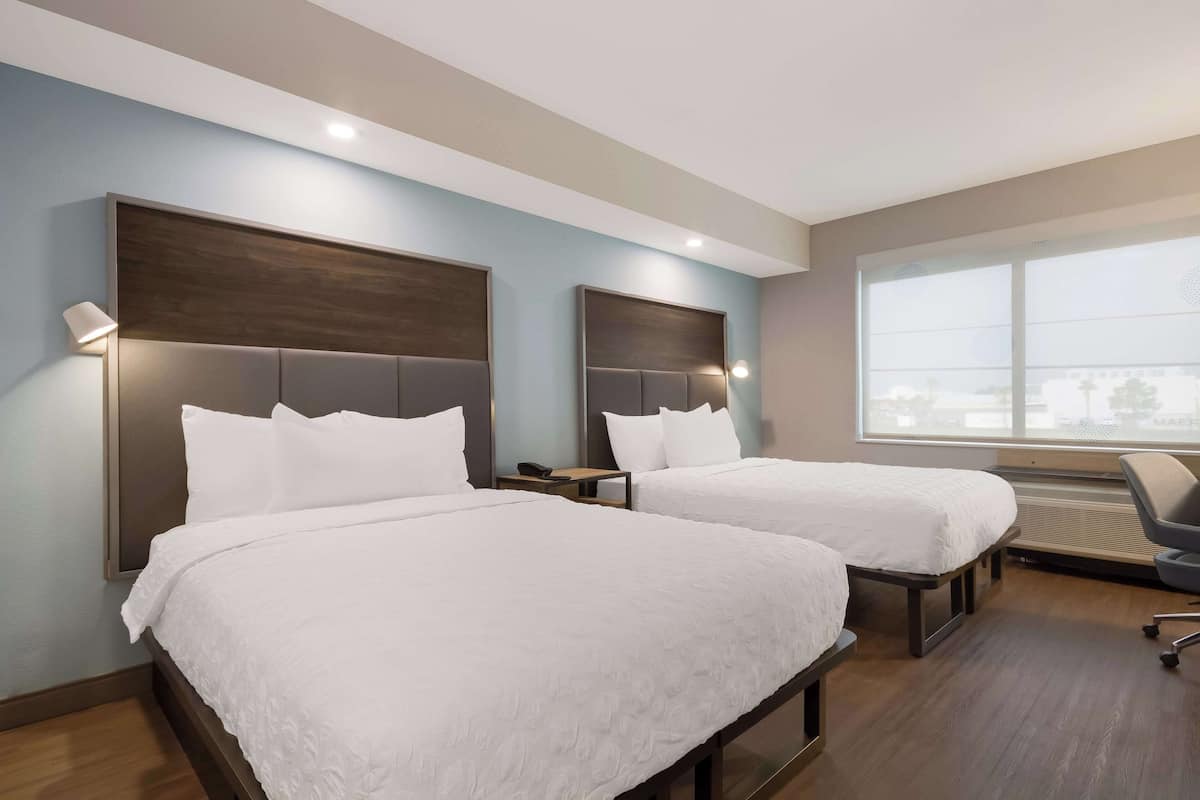 A hotel room with two beds, a large window, and a modern design.