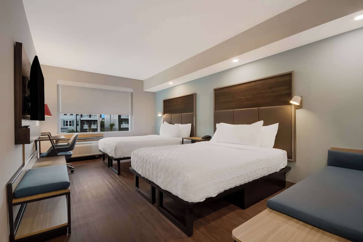 A hotel room with two beds, a desk, a chair, and a TV.