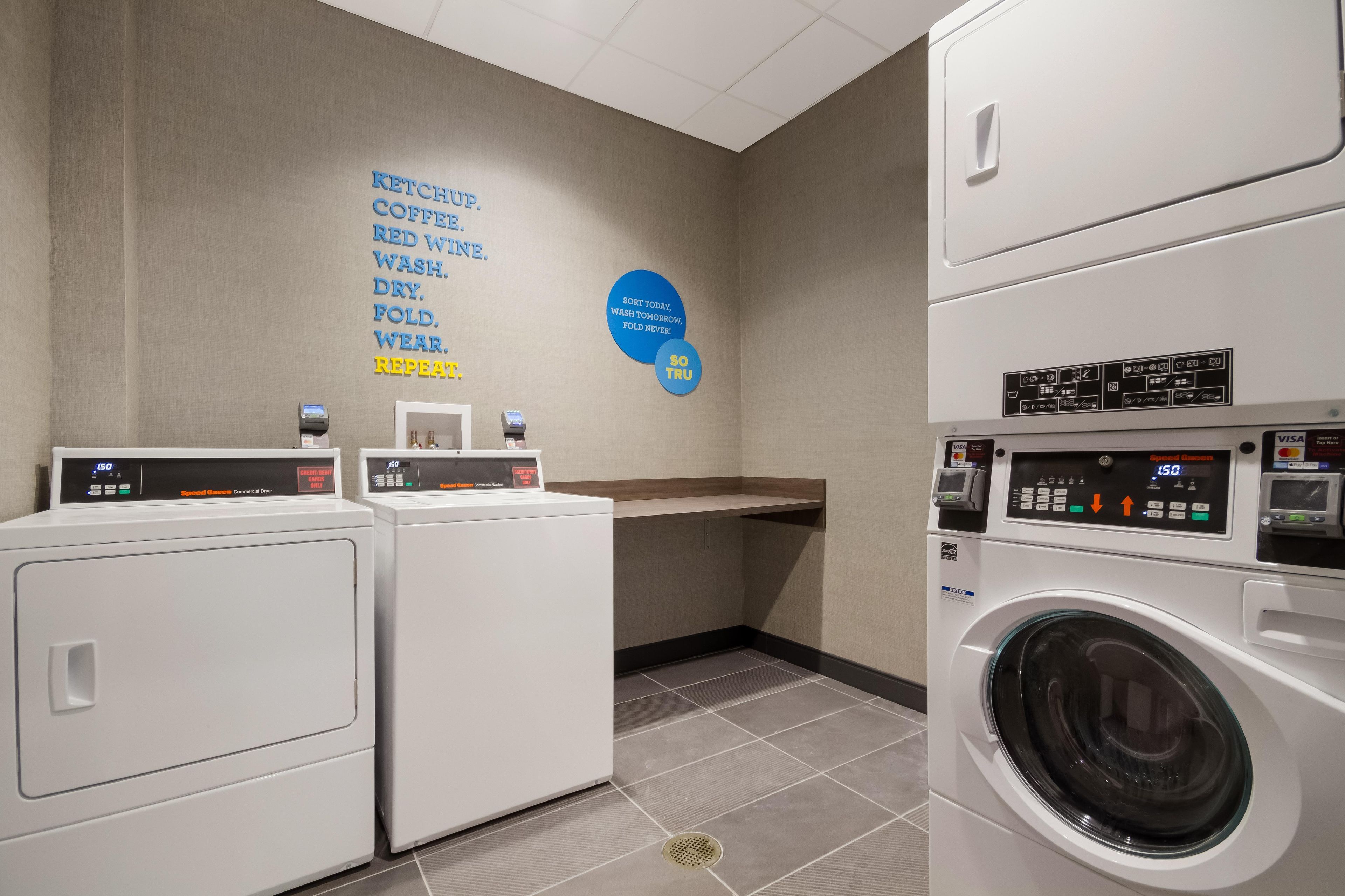 A laundry facility with multiple washing machines, a commercial dryer, and a wall with instructions for use.