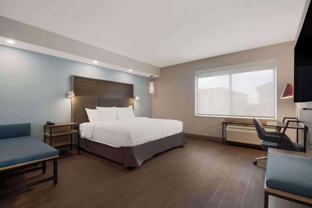 A hotel room with a bed, a desk, and a chair. There is a window with a view of buildings.
