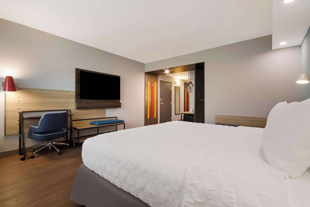 A hotel room with a large bed, a desk with a chair, a flat-screen TV, and a mirror.