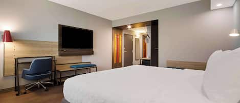 A hotel room with a large bed, a desk with a chair, a flat-screen TV, and a mirror.