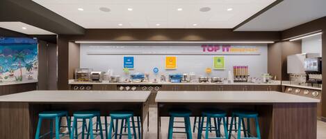 A modern breakfast area with a central island, bar stools, and a variety of breakfast options displayed.