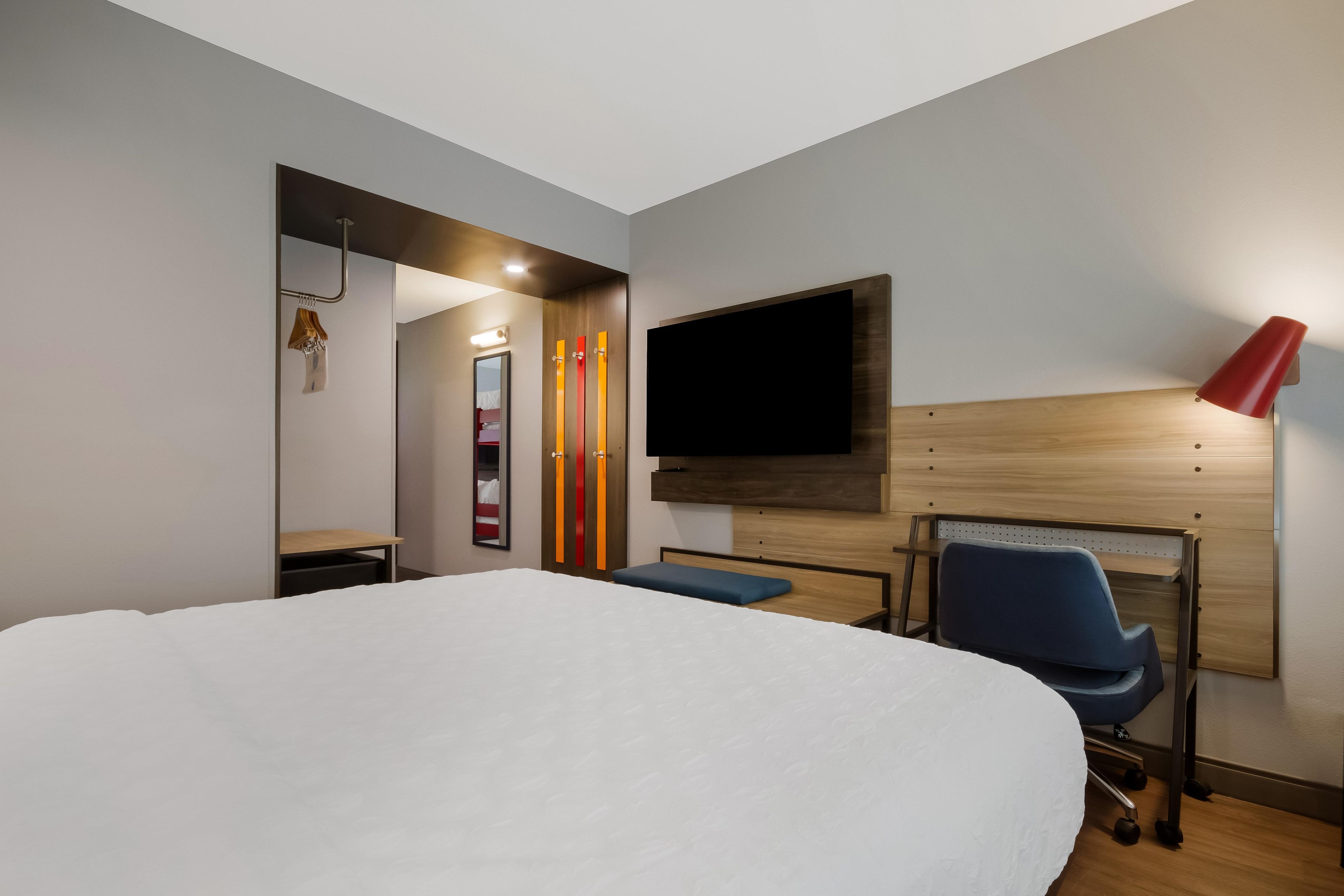Ein Hotelzimmer mit einem großen Bett, einem Schreibtisch, einem Stuhl, einem an der Wand befestigten Fernseher und einer Nachttischlampe.