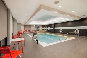 A swimming pool with red chairs and tables, a lifeguard stand, and a ceiling with recessed lighting. - Tru By Hilton Destin (Destin)