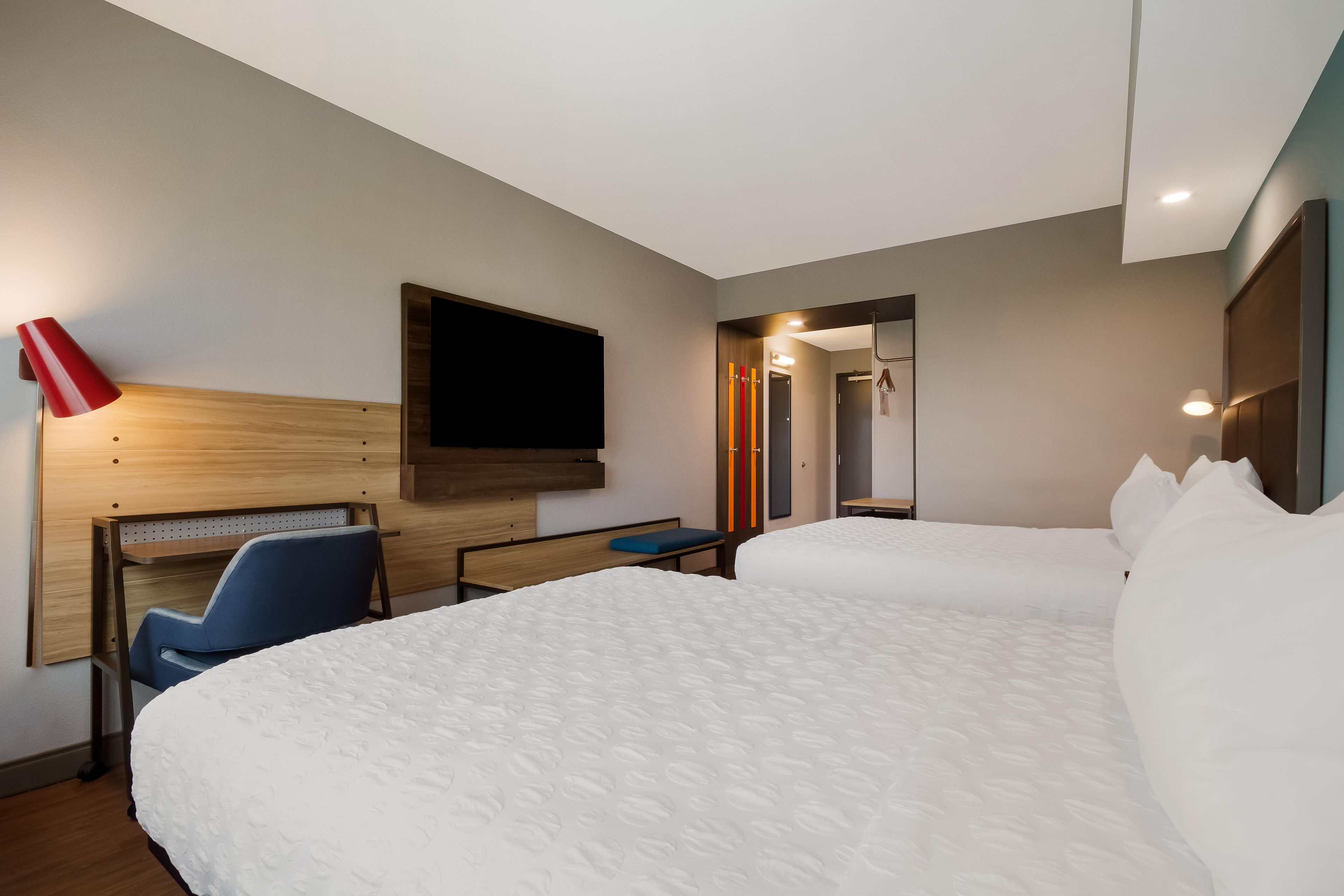 Une chambre d’hôtel avec deux lits, un bureau, une chaise, une télévision et un espace douche.
