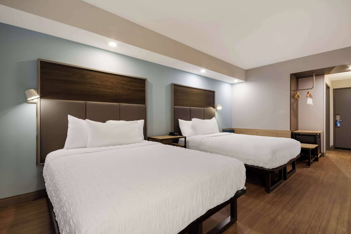 A hotel room with two beds, a desk, and a chair.