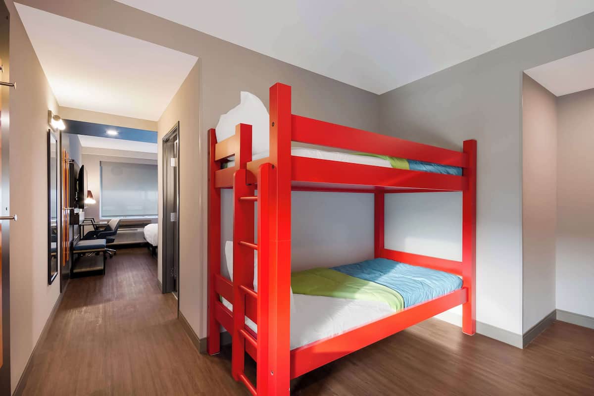 A bunk bed room with a wooden floor, a desk with a chair, and a mirror.