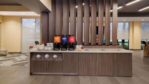 Un área de recepción moderna con un mostrador central, varios dispensadores de café y vistas al exterior a través de amplias ventanas.