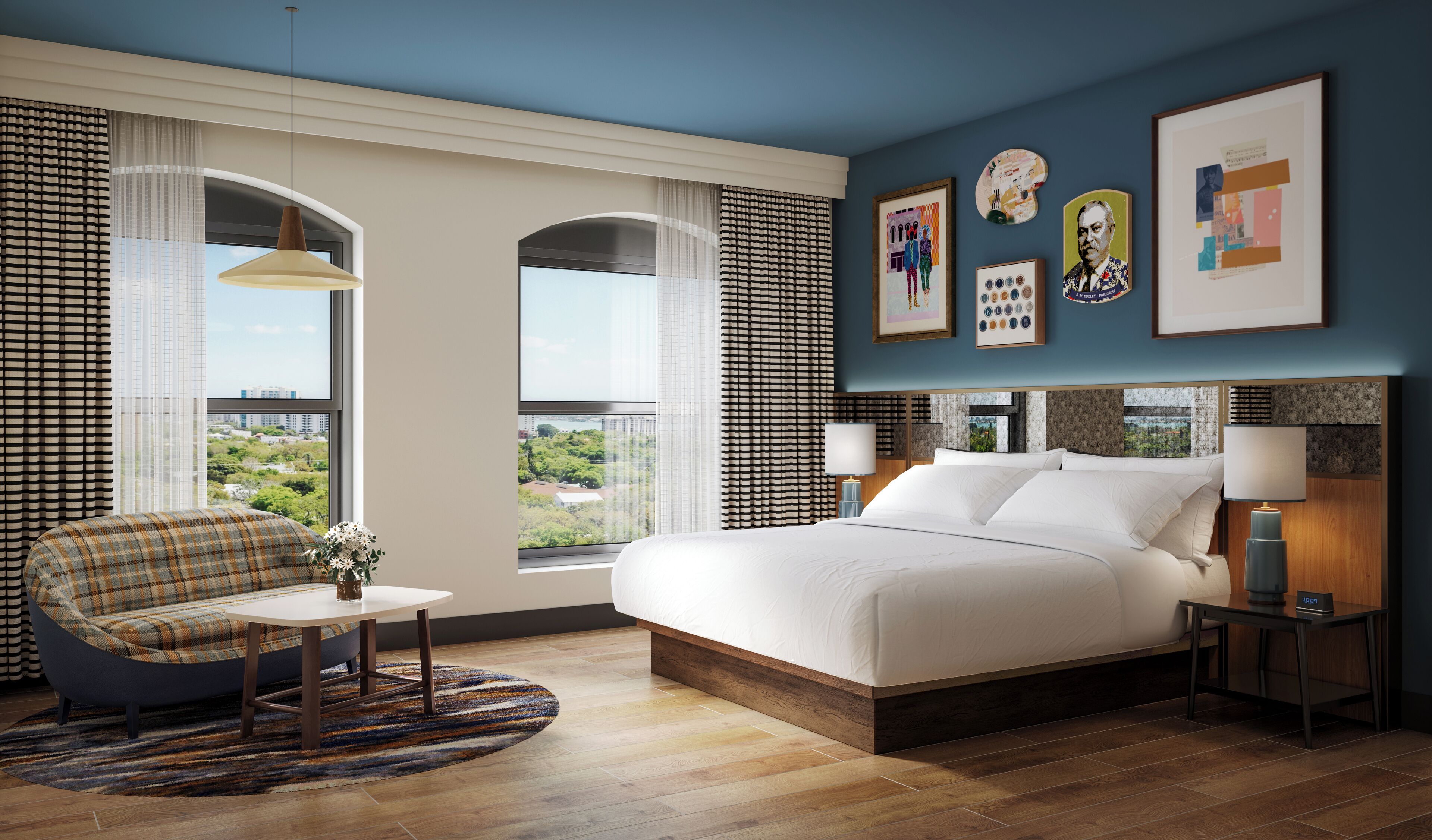 Une chambre d’hôtel moderne avec un grand lit, un canapé, une petite table et des œuvres d’art accrochées aux murs.