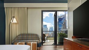 A hotel room with a bed, a sofa, a TV, a balcony with a city view, and a large window. - The Untitled Nashville Hotel, Tapestry Collection by Hilton (Nashville)