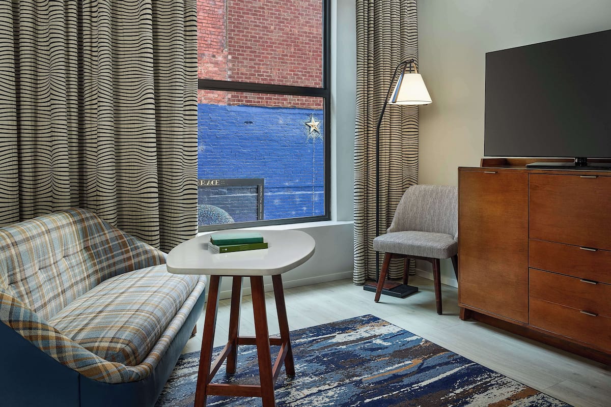 A modern living room with a sofa, a small table, a chair, a TV, and a view of a blue wall outside.