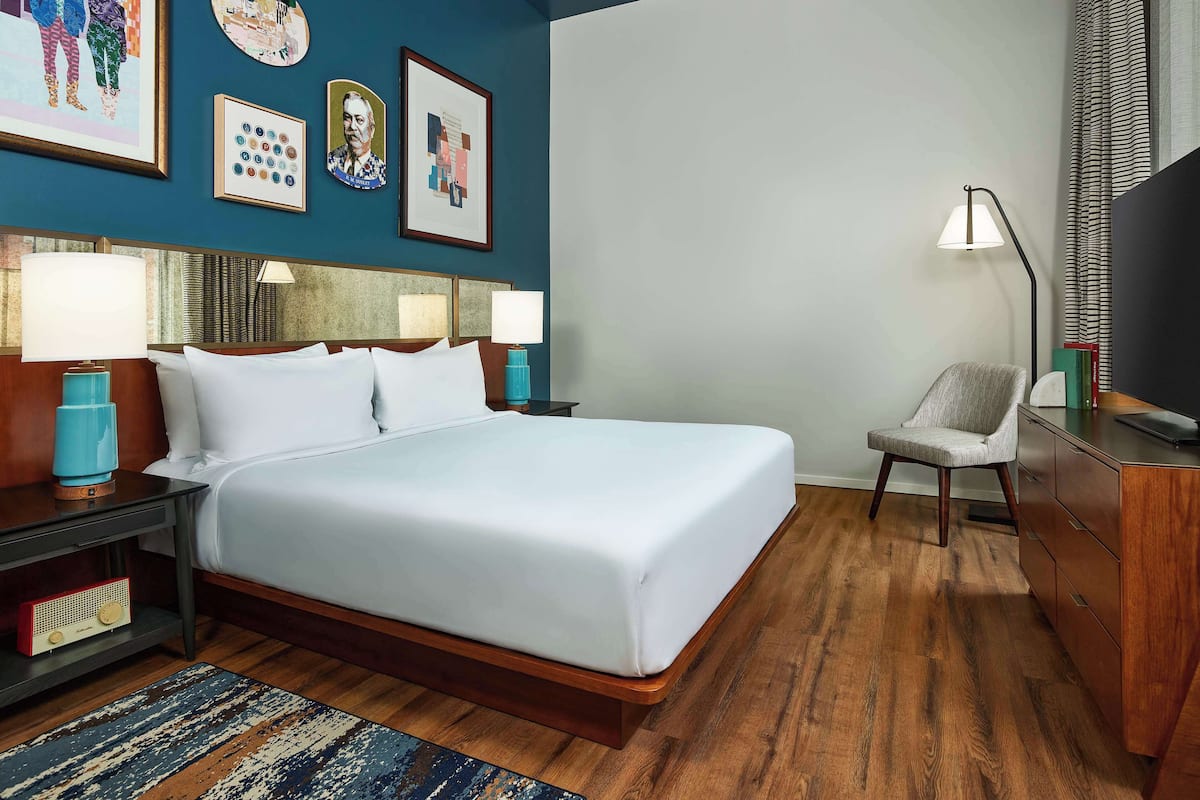 A hotel room with a large bed, bedside tables with lamps, a chair, a desk, and a television.