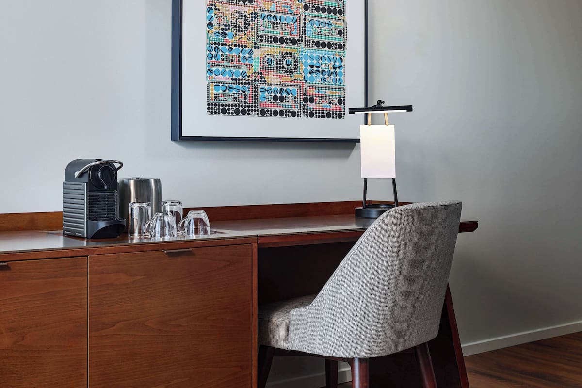 A modern desk with a coffee maker, glasses, and a framed abstract art piece above it.