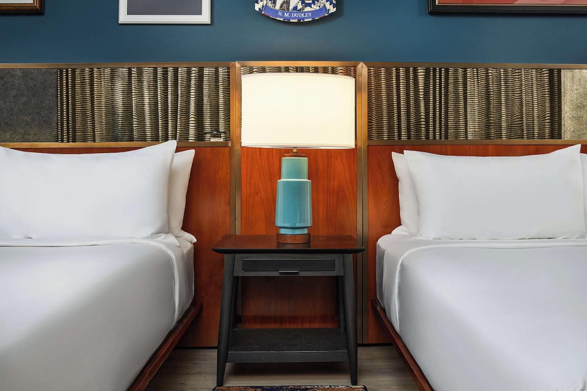 A hotel room with two beds, a nightstand with a lamp, and a decorative wall plaque.