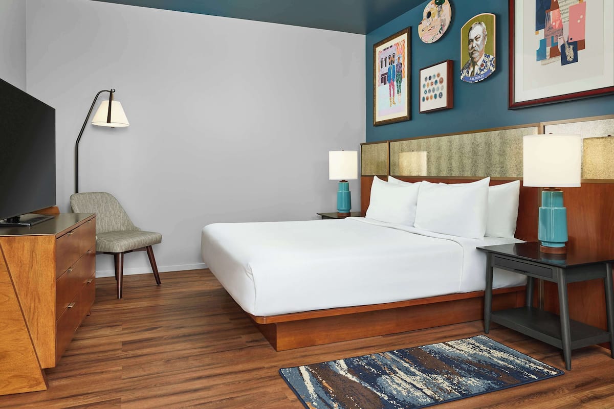 A hotel room with a bed, a desk, a chair, and a desk lamp.