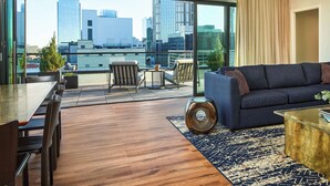 A modern living room with a large window, a sofa, a coffee table, and a dining area with chairs and a table. - The Untitled Nashville Hotel, Tapestry Collection by Hilton (Nashville)