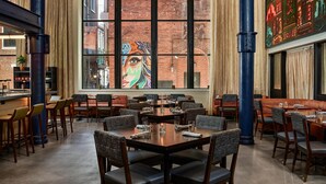 A restaurant with high ceilings, large windows, and a mural on the wall. - The Untitled Nashville Hotel, Tapestry Collection by Hilton (Nashville)