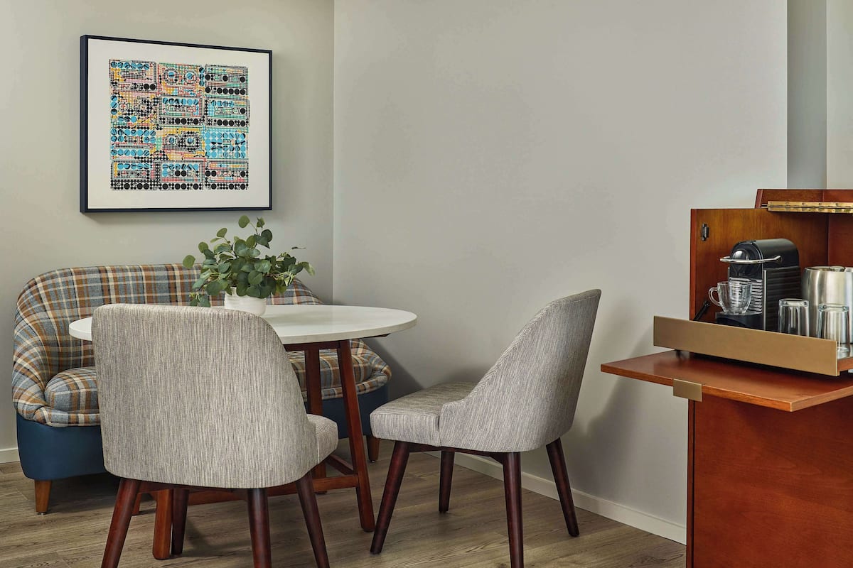 A dining area with a round table, two upholstered chairs, a plaid sofa, and a coffee station with a coffee maker and cups.