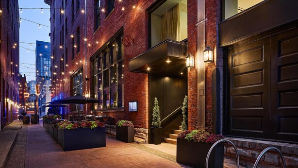 A brick building with a dark garage door, outdoor seating, and a staircase leading to the entrance. - The Untitled Nashville Hotel, Tapestry Collection by Hilton (Nashville)