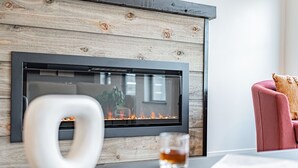 A modern living room with a fireplace, a glass of whiskey, and a red armchair. - Basecamp Stays: Stylish Home - Hot Tub, AC, Garage (Driggs)