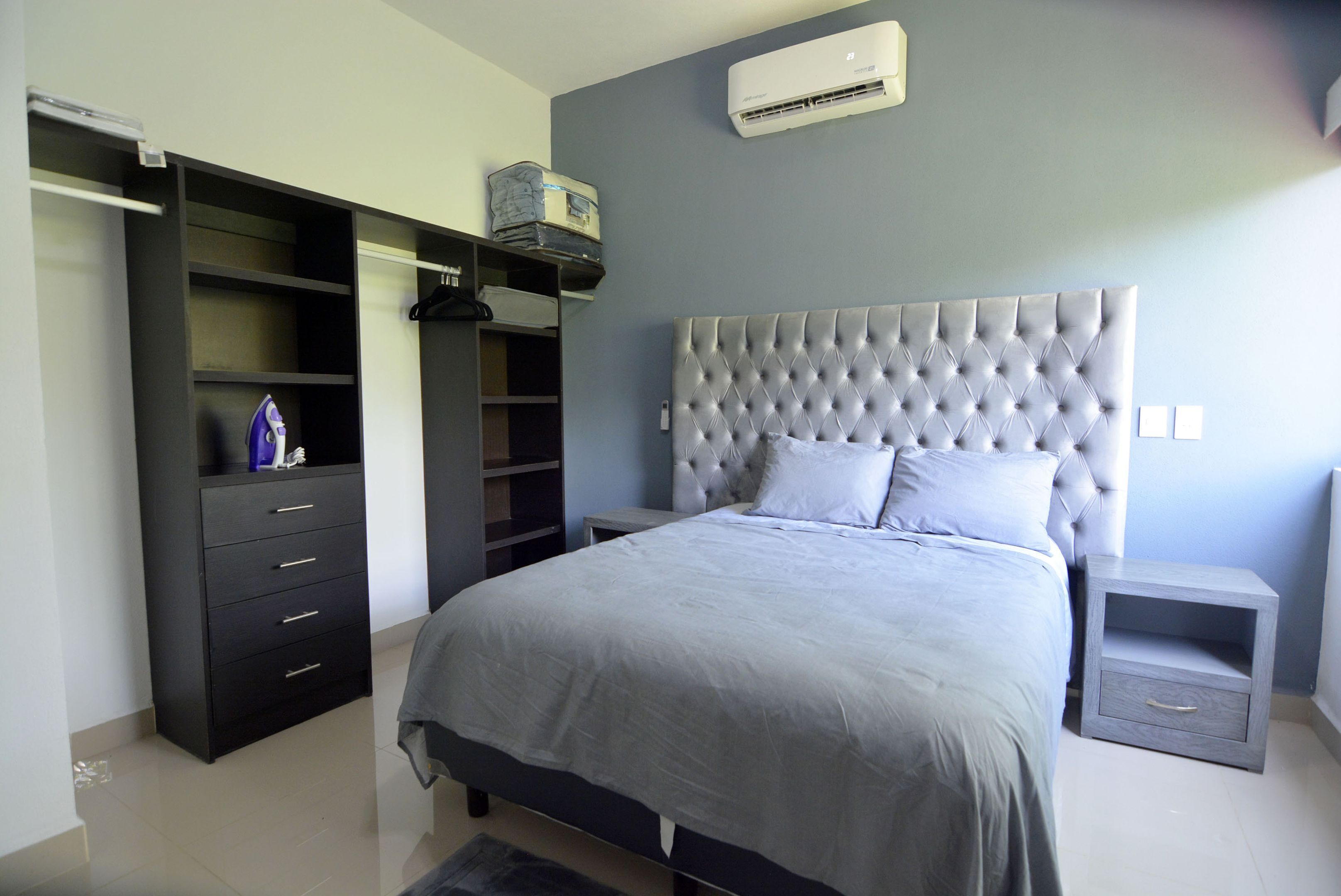 Een slaapkamer met een groot bed, een kledingkast, een nachtkastje en een airconditioning op de muur.